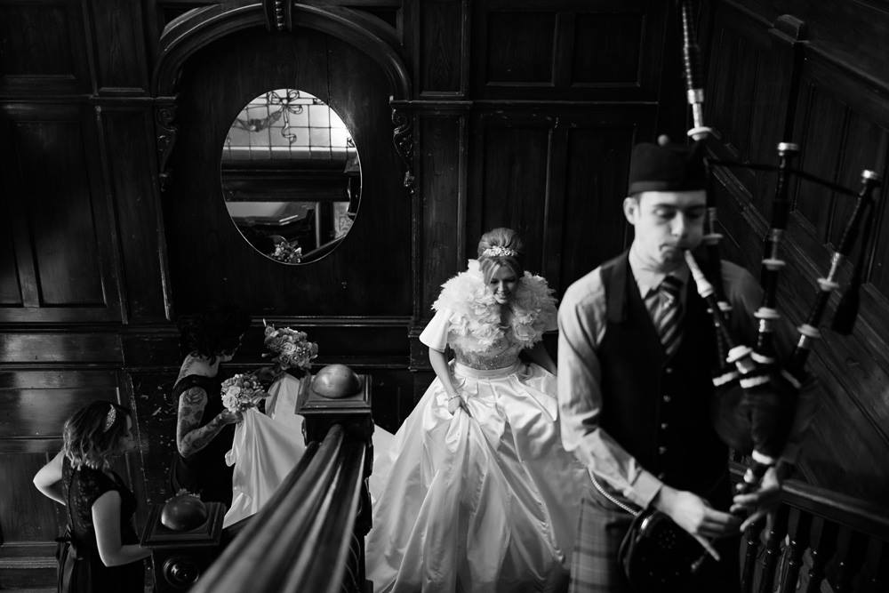 Scottish Piper Hire playing bagpipes whilst marching up stairs in front of a bride inside a reception venue Sloans, Glasgow.