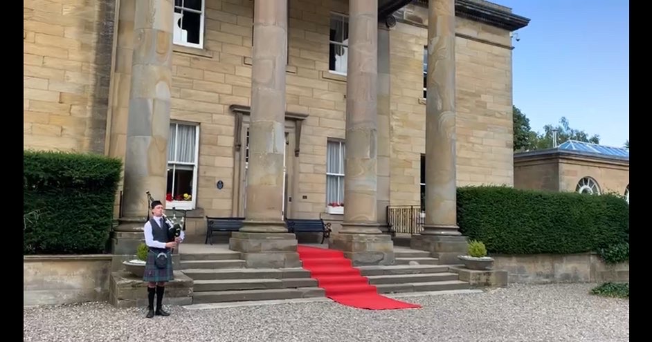 Scottish Piper Hire in traditional highland dress playing bagpipes in front of Balbirnie House