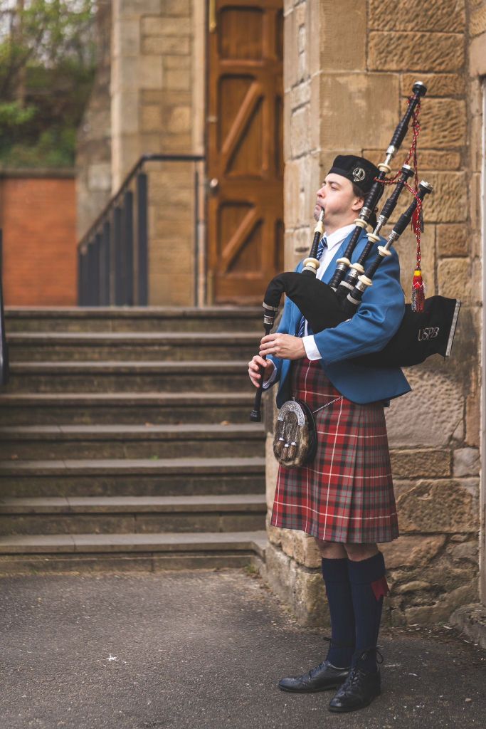 Scottish Piper Hire playing bagpipes outside a church for guests arriving to the venue.