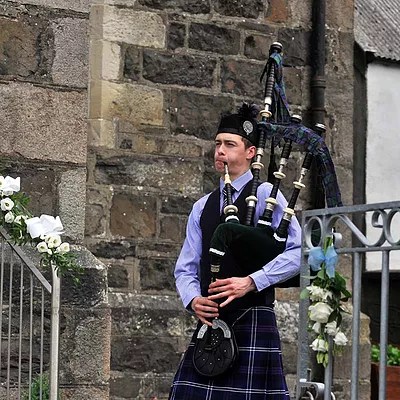Scottish Piper Hire playing bagpipes outside a church for guest arriving to a wedding.