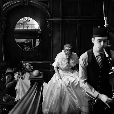 Scottish Piper Hire playing bagpipes whilst marching up stairs in front of a bride inside a reception venue Sloans, Glasgow.